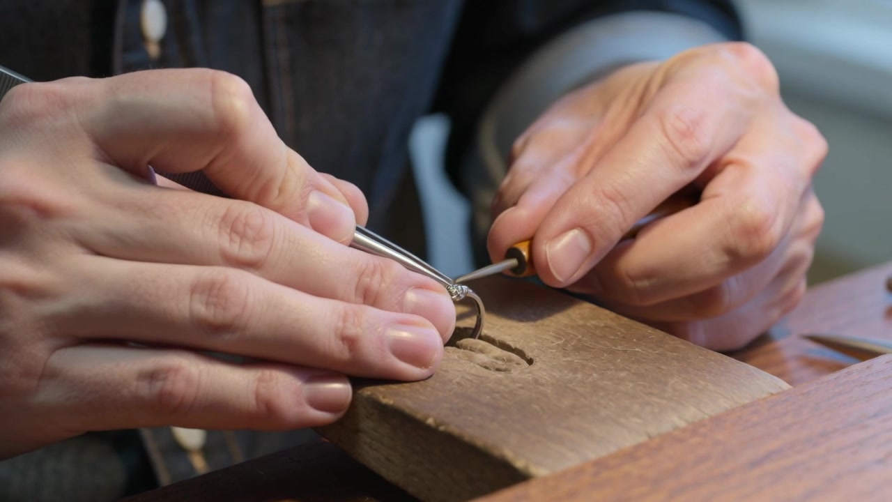 Placing ring on bench pin jeweler hands with denim sleeve pressing tool securing stones by window