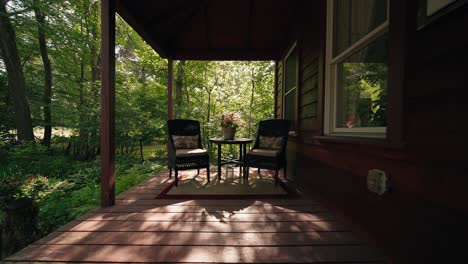 Push-in-shot-of-two-chairs-on-a-farmhouse-porch-during-a-sunlit-summer-morning,-with-warm-backlighting