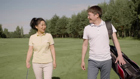 Man-and-woman-with-golf-apparel-have-a-conversation-while-cross-the-field