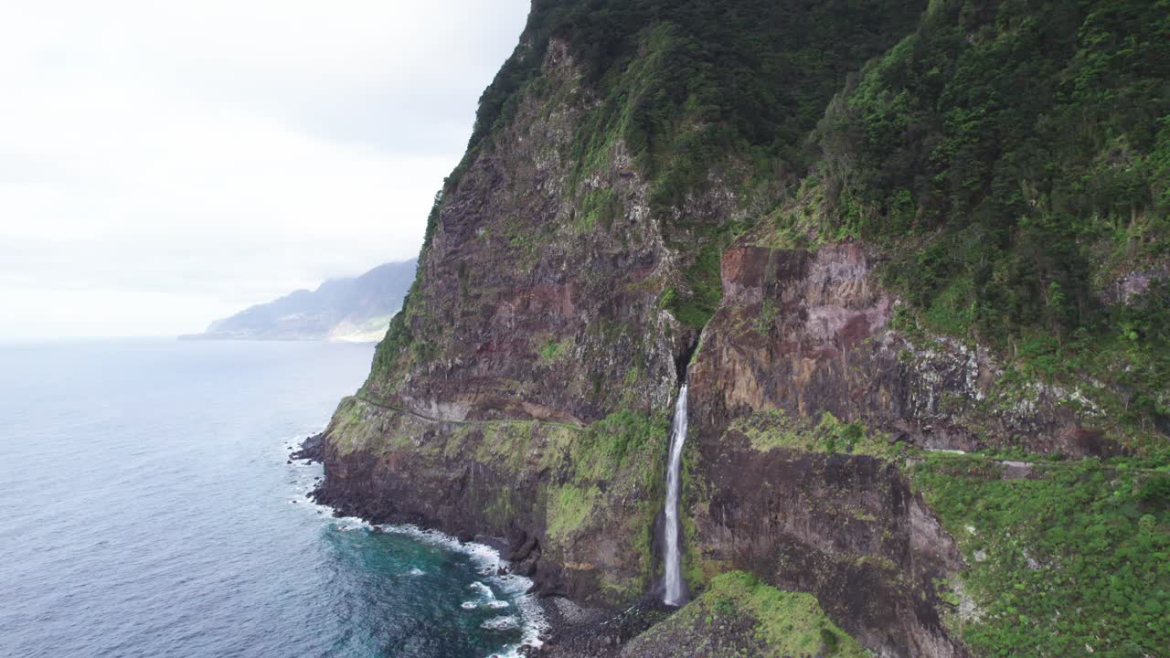 포르투갈의 마데라에서 바다로 흘러내리는 절벽의 폭포, 세이 마을 근처의 배경에는 산이 있습니다.
