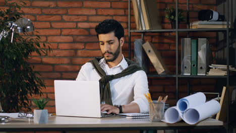 young arabian architect working on new project with laptop sitting at desk in his office