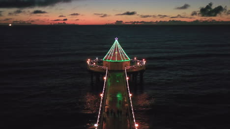 Roundhouse Aquarium With Christmas Lights During Christmas Season At Sunset In Manhattan Beach Pier In USA. - aerial pullback shot