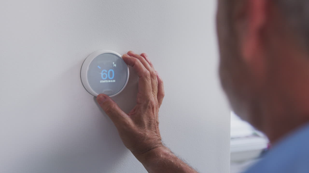 Senior Hispanic Man Adjusting Digital Central Heating Thermostat In Home