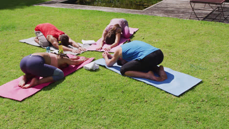 diverse group practicing yoga, kneeling on mats and stretching in sunny park