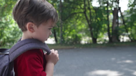 slow motion video of a young little boy in a red t-shirt walking with backpack