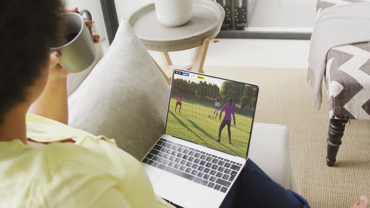 mulher afro-americana usando laptop com vários jogadores de futebol masculino jogando partida na tela