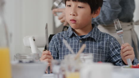 happy little asian boy eating fresh waffles for breakfast enjoying delicious homemade meal with family in kitchen at home 4k