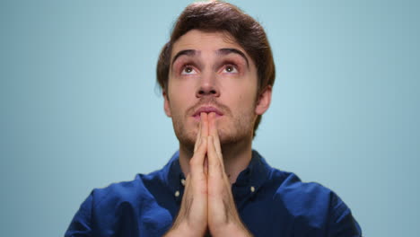 Handsome-man-praying-in-studio.-Serious-guy-holding-hands-in-prayer-position