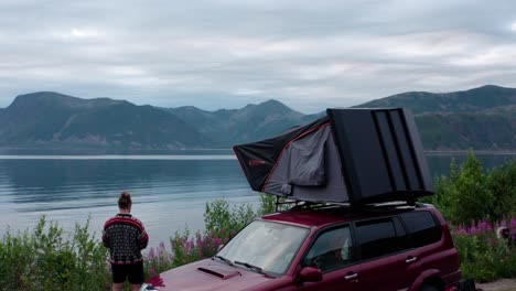 a man standing next to a car with roof tent in sifjord camping ground, norway