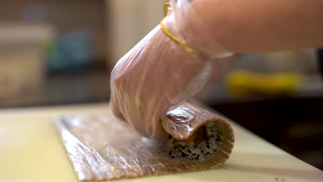 a cook uses rolling mat in order to roll all the ingredients, namely rice, cheese and salmon together to create sushi roll