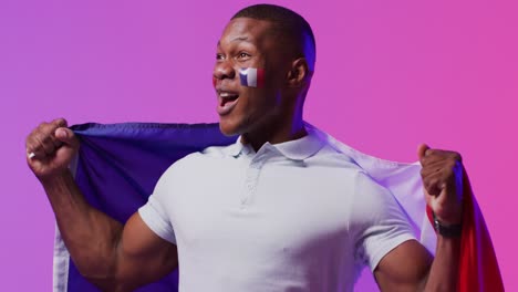 happy african american male football supporter with flag of france over pink lighting
