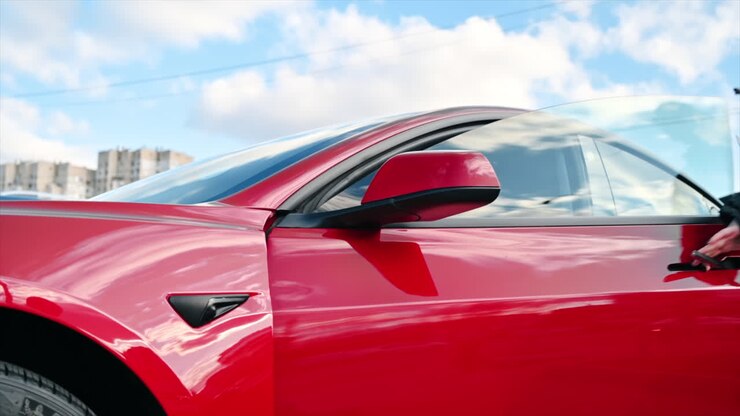 Primo piano di una donna che apre la sua auto elettrica rossa con una tessera e sale a bordo. Rallentatore
