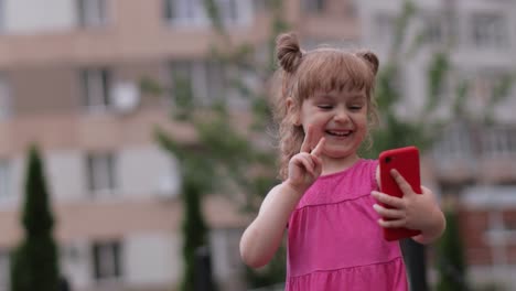 Niña-Hablando-Por-Teléfono-Inteligente-Al-Aire-Libre.-Un-Niño-Vestido-De-Rosa-Hablando-Por-Teléfono-Móvil-En-Las-Calles-De-La-Ciudad