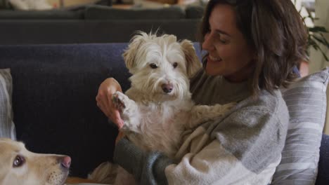 Smiling-caucasian-woman-cuddling-her-pet-dog-sitting-on-sofa-at-home