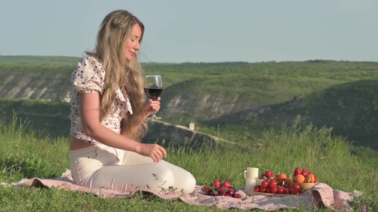 Woman drinking red wine with fruit at a picnic in nature