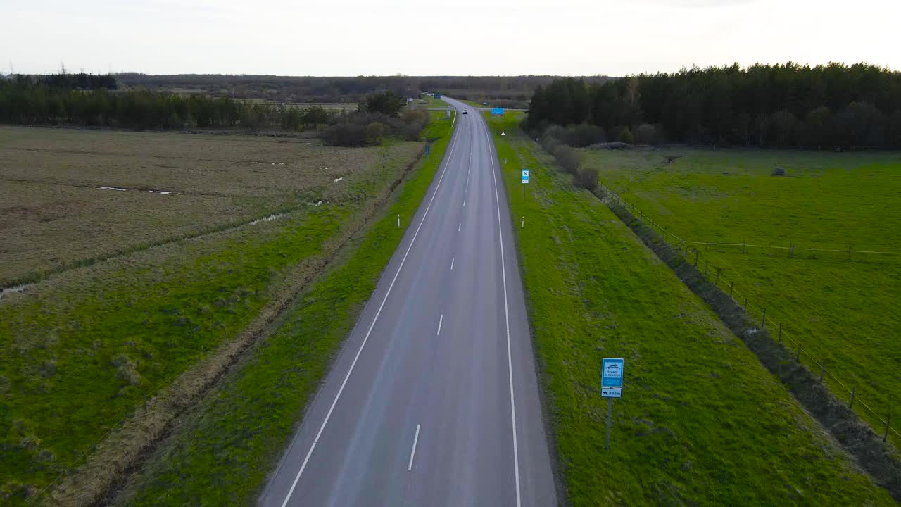 Flying forward over rural asphalt motorway while cars driving on Parnu highway through forest and green fields. Drone flying above long smooth flowing traffic, wide view moving along evening road