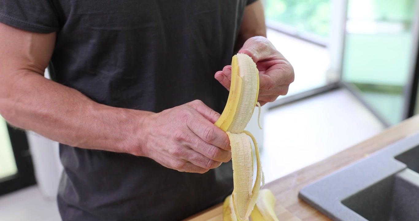 Giovane uomo inizia a sbucciare una banana matura in una cucina moderna