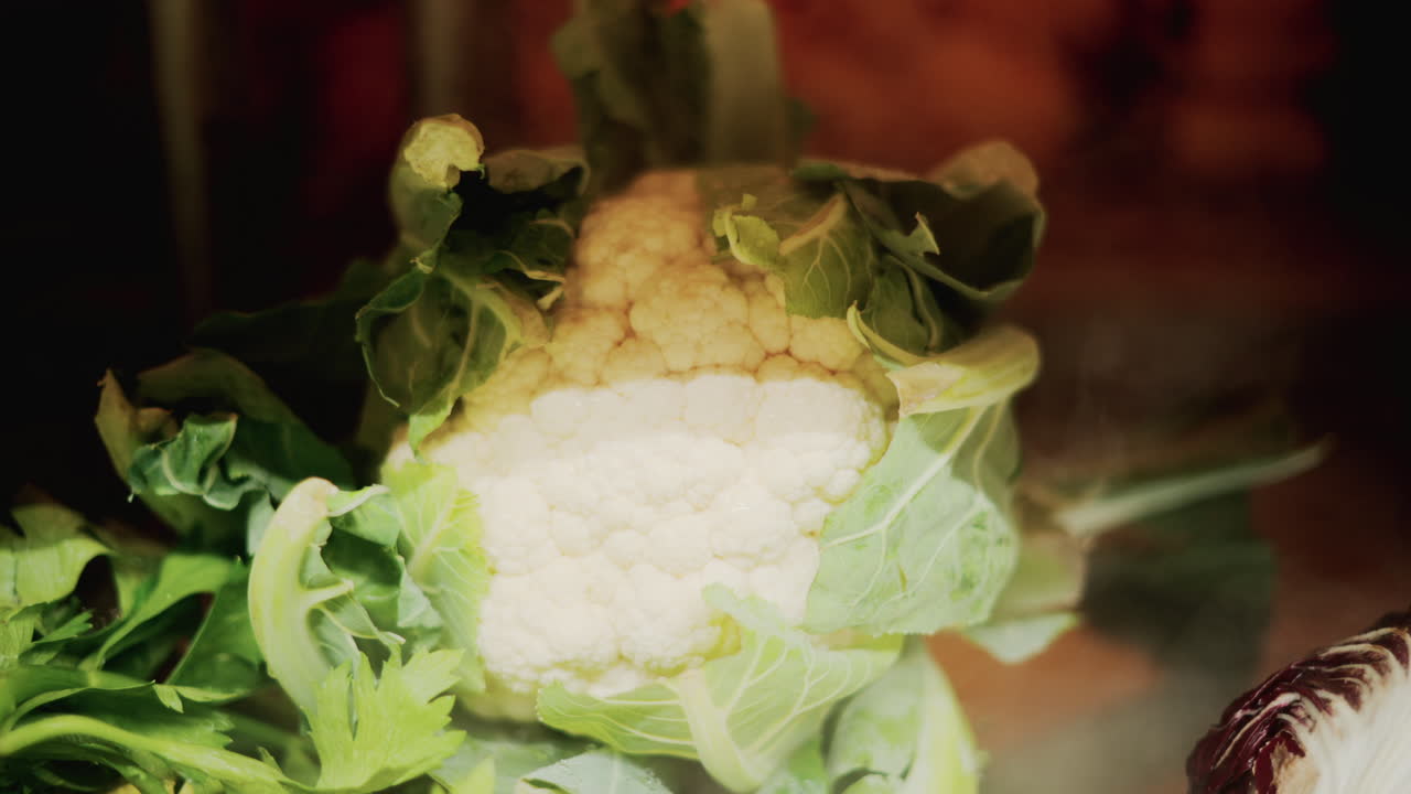Close up of a fresh cauliflower surrounded by green leaves under warm light