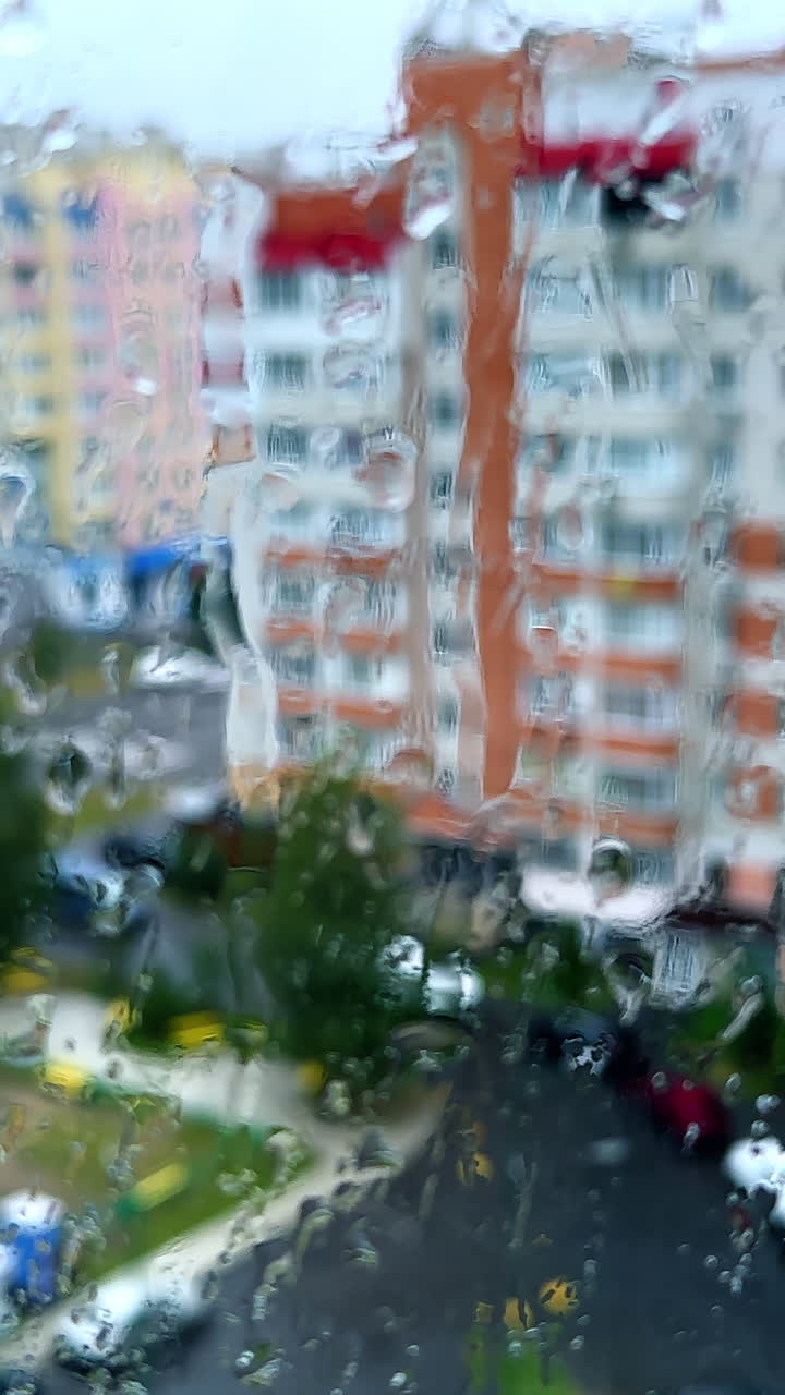 Window covered with rain drops. Blurred image of colorful multistoried building at backdrop.. Vertical video