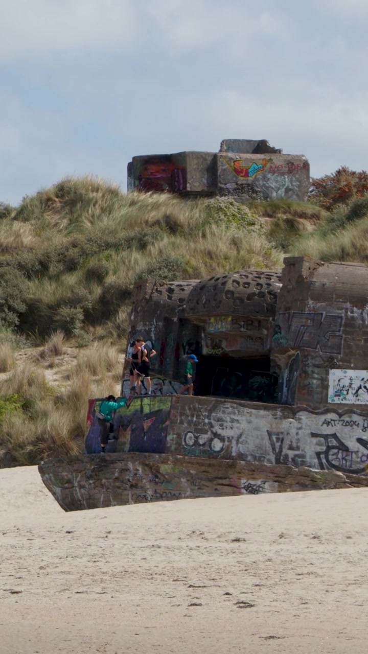 Una ripresa verticale di un bunker di cemento abbandonato con graffiti colorati su una spiaggia sabbiosa.