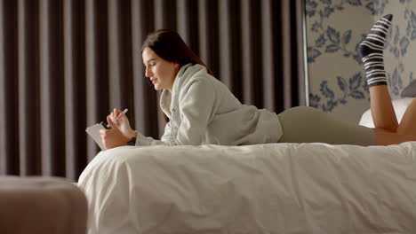 relaxing on bed, woman holding tablet and talking in cozy home setting