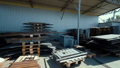 covered outdoor warehouse. shelves with metal sheets, square pipes, fittings. wooden euro pallets with finished products