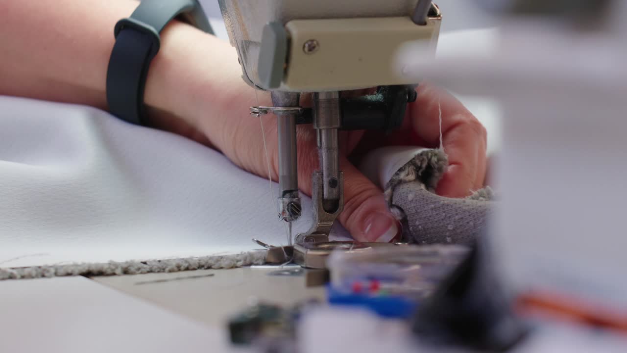 Detailed view of an industrial sewing machine stitching fabric. A person is working with precision, creating clean seams for textile production