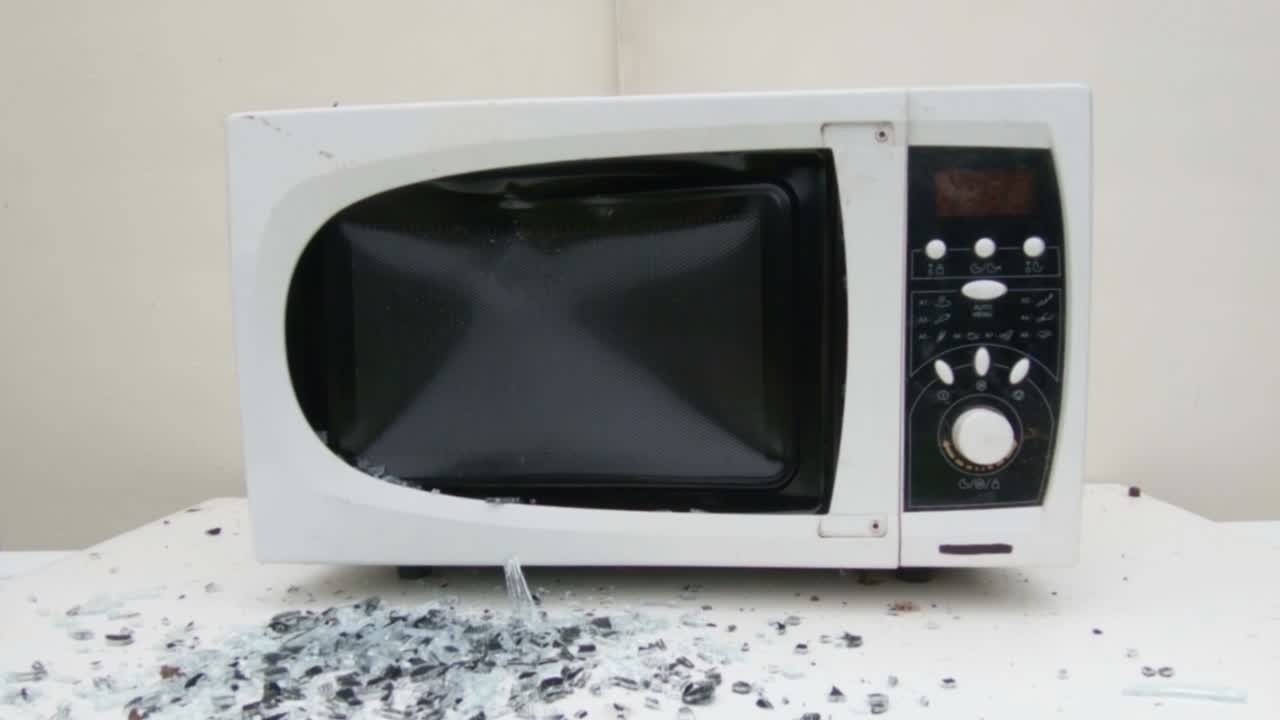 검은 금속 망치가 오래된 전자레인지를 부순다