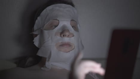 young woman in regenerating sheet mask lies in dark room