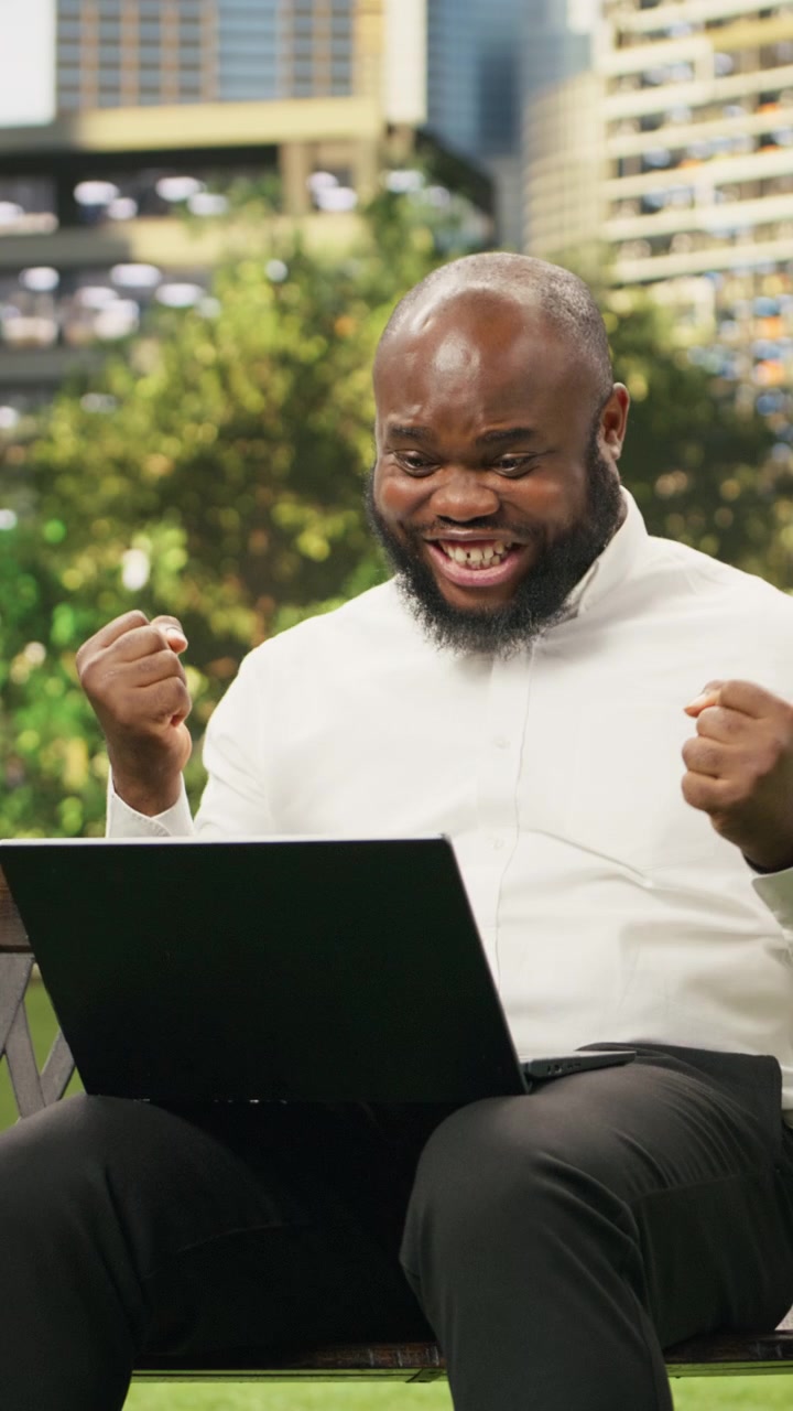 Vertical Video Excited businessman raising clenched fists while looking at laptop