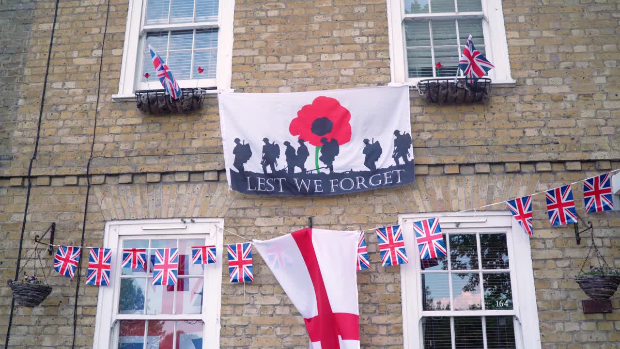Lest we forget and England flags hanging outside of the house commemorating VE Day also known as Victory in Europe during a windy day