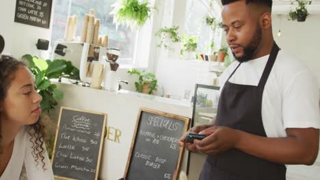 happy biracial female client paying for order with smartphone at cafe