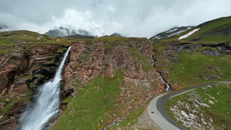 a beautiful waterfall cascading down rocky cliffs with green hills in the background, aerial view