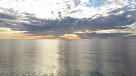 AERIAL:-Pan-Shot-of-Flying-Above-Baltic-Sea-During-Golden-Hour-with-Majestic-Horizon-with-Orange-and-Blue-Colours-in-the-Sky