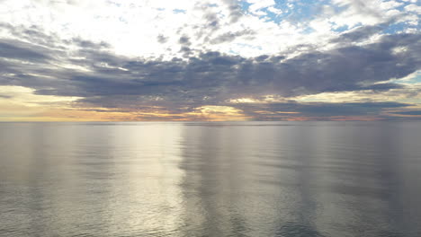 aerial: pan shot of flying above baltic sea during golden hour with majestic horizon with orange and blue colours in the sky