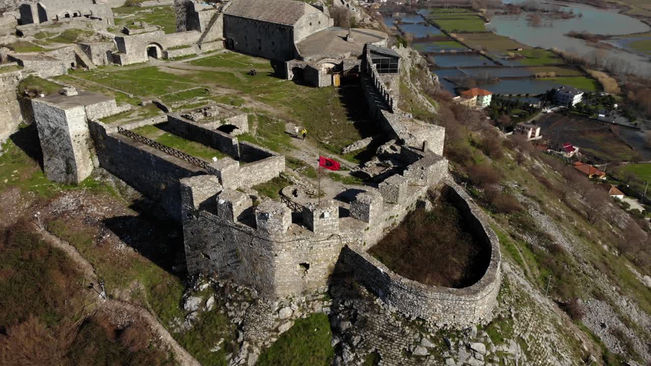 Vakkert slott med steinvegger bygget på en bakketopp, omgitt av jorder og elv i Shkoder, Albania