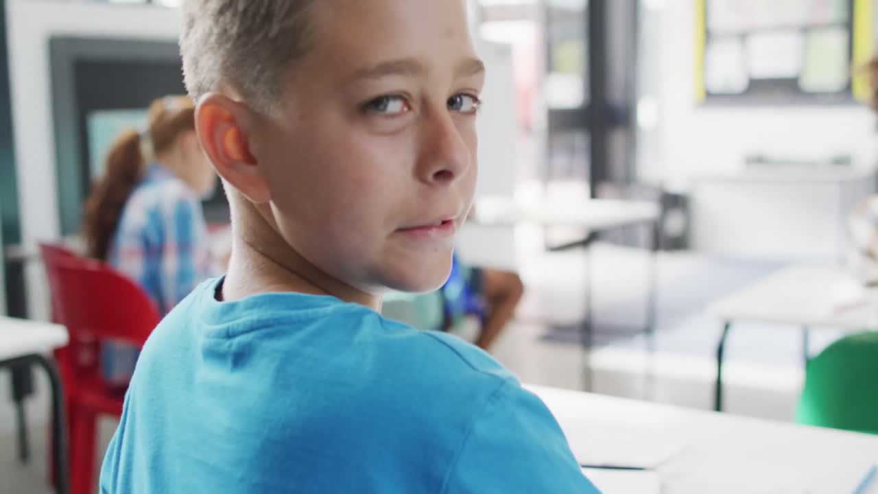 портрет счастливого белого школьника за столом, поворачивающегося и улыбающегося в школьном классе.