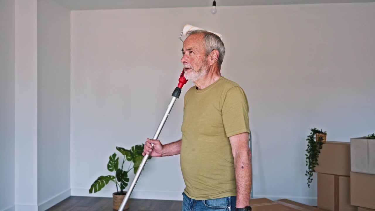 Uomo anziano pensieroso con rullo da pittura nella nuova casa