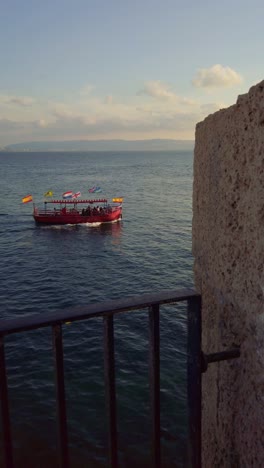 red tourist boat sailing in the mediterranean sea near acre old city, israel