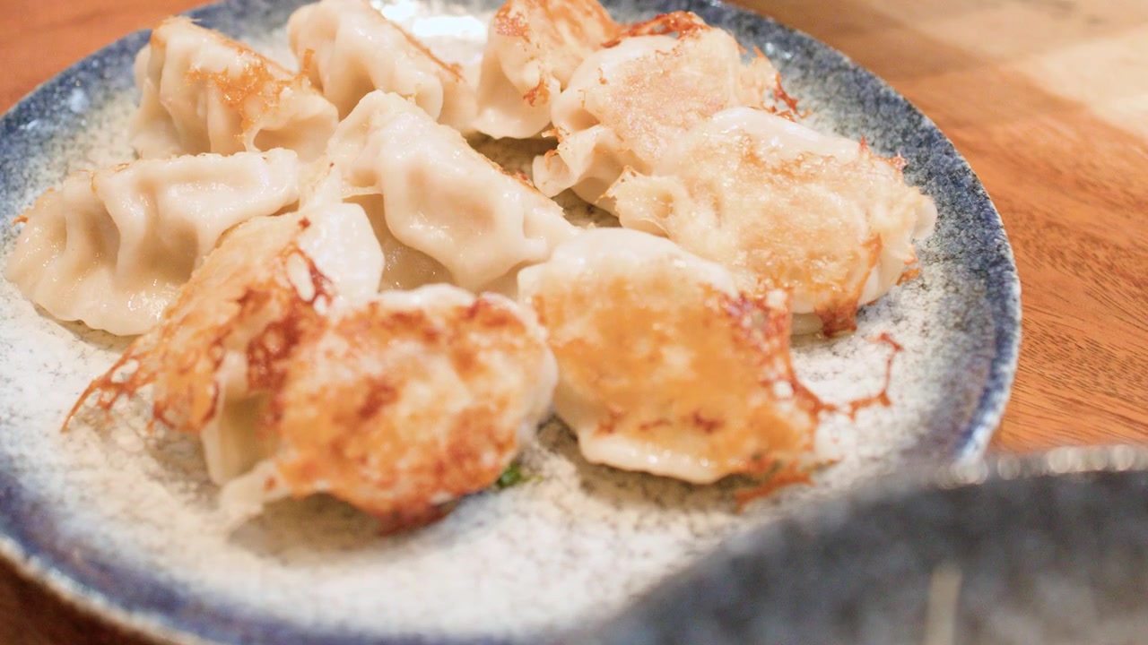 Close-up shot of golden crispy pan-fried dumplings served on a rustic ceramic plate.