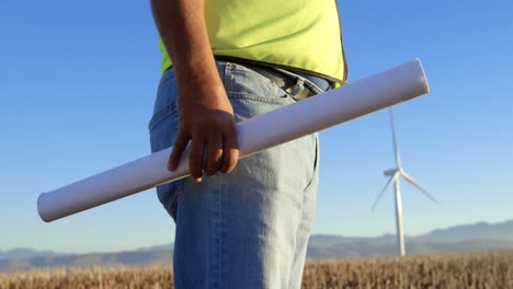 Male-engineer-standing-with-blueprint-in-the-wind-farm-4k