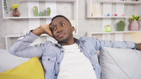 thoughtful happy african young man sitting alone on sofa at home.