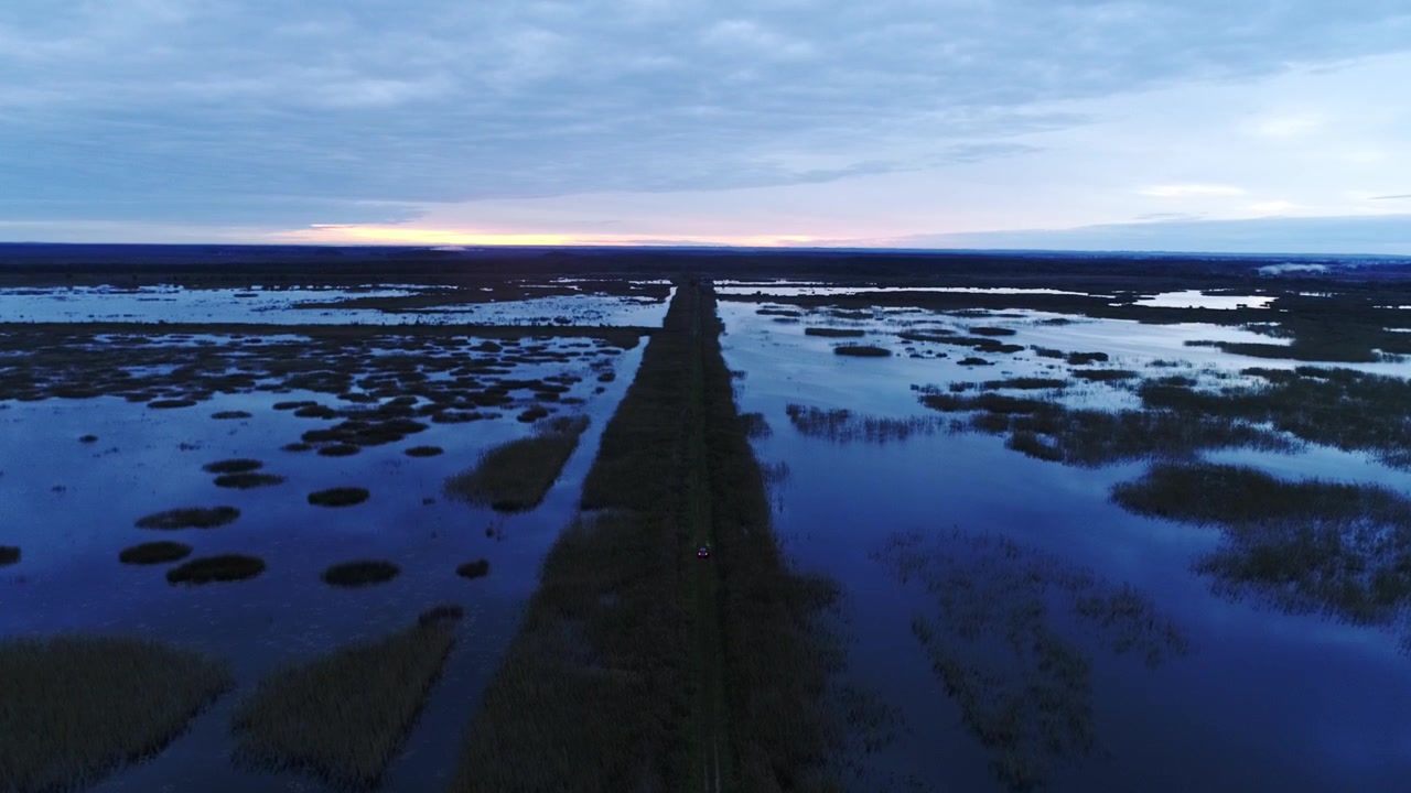 Zmierzch ukazuje zalane bagna Łatgalii, podzielone przez odległą, prostą polną drogę.