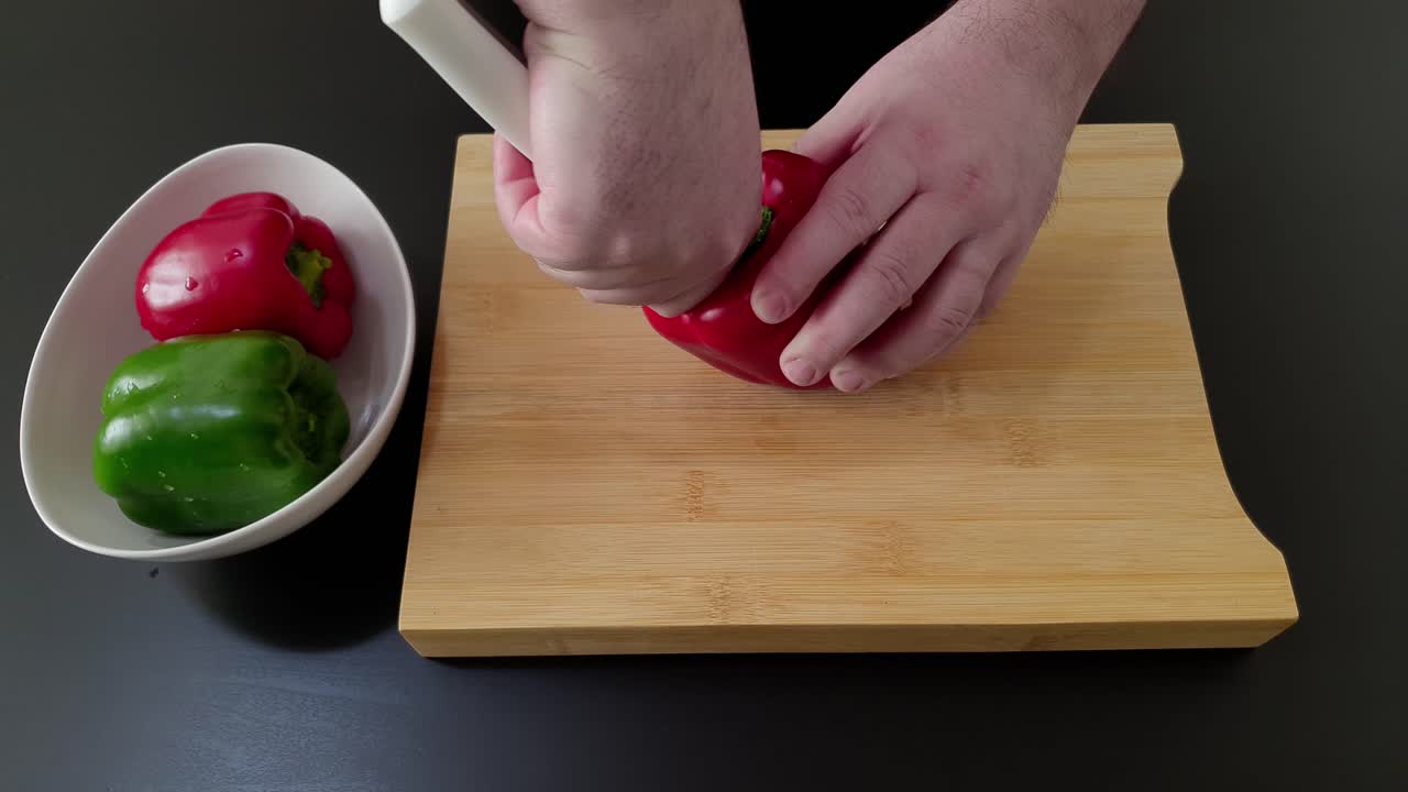 manos masculinas cortando pimientos dulces rojos y verdes en una tabla de cortar de madera para un plato saludable - tiro en ángulo alto, de cerca