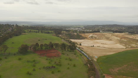 The-camera-captures-an-aerial-view-of-a-train-running-between-a-green,-lush-landscape-and-an-open-pit-mine,-presenting-a-picturesque-scene