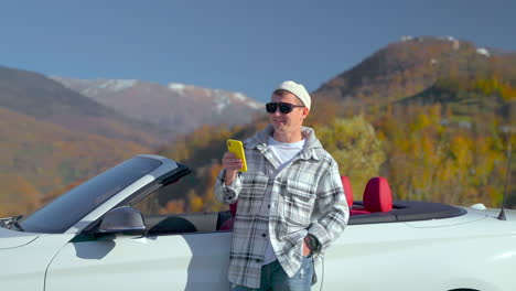 man using phone in a convertible car with an autumnal view