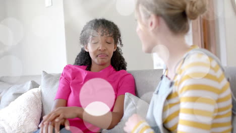 Animation-of-light-spots-over-two-diverse-teenage-girls-talking-on-couch