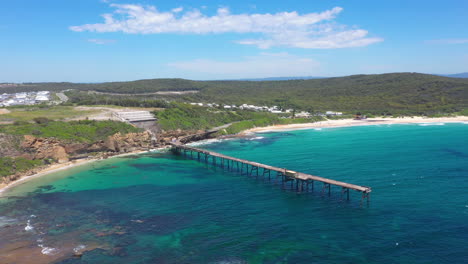 Beautiful-pier-in-tropical-Australian-coastal-bay,-turquoise-water-aerial-reveal