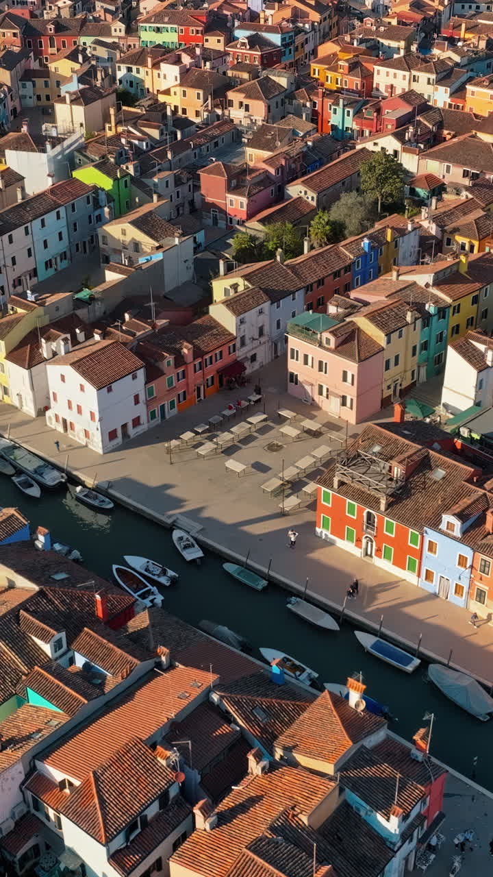 Aerial drone view of boats on the sides of a canal near the colourful houses of Burano. Vertical