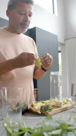 vertical video of senior biracial man preparing smoothie in kitchen at home